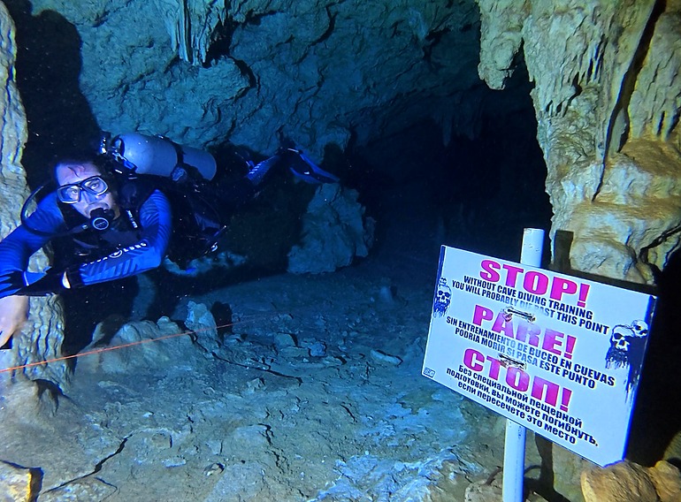 Guided cavern diver following the line before the cave-training warning sign