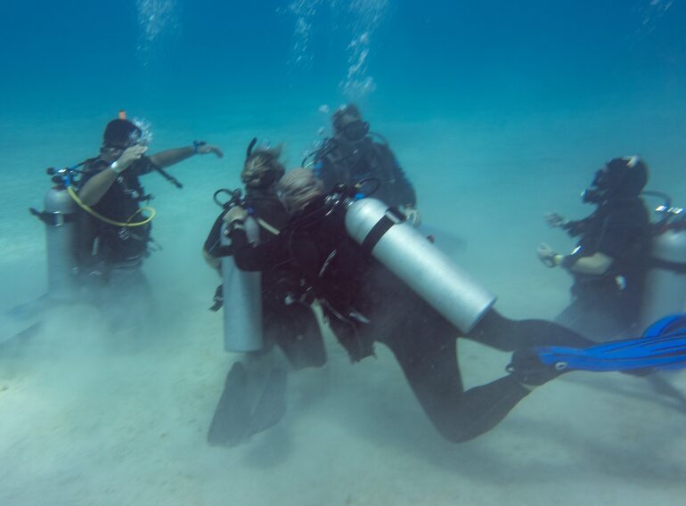 Divemaster candidates practising demonstration-quality scuba skills with an instructor in shallow water